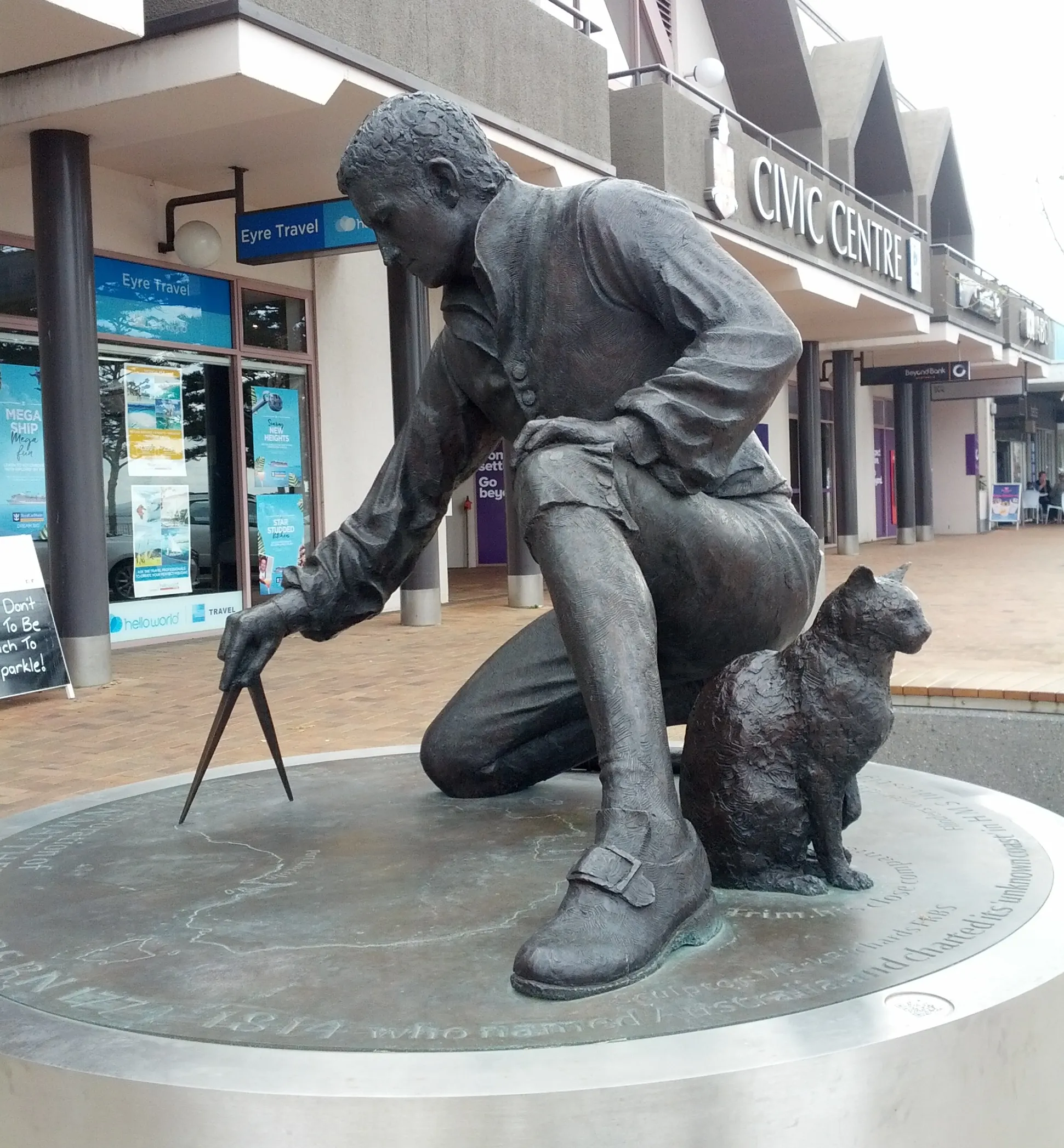 Escultura de bronce de Matthew Flinders arrodillado mientras traza un mapa, acompañado por su gato Trim sentado a su lado. El monumento se encuentra en Port Lincoln, Australia Meridional.